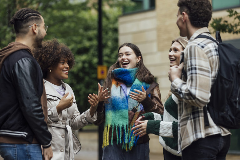 A small group of university students standing together talking in the city on an autumn day.