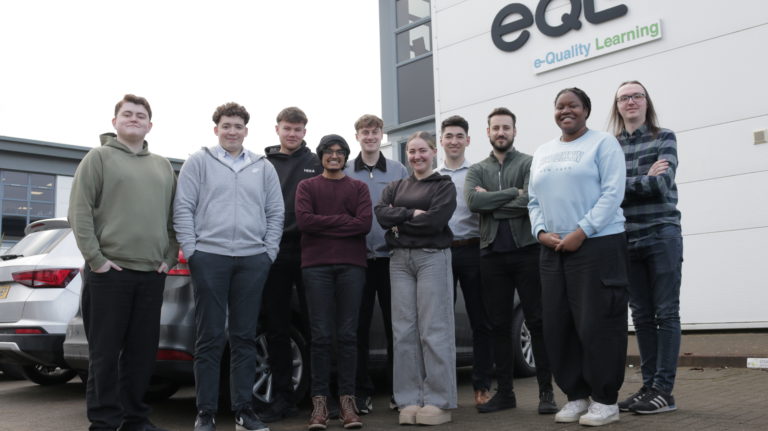 A photo of ten apprentices stood outside the eQS office. There are eight male apprentices and two female apprentices. They are all smiling at the camera.