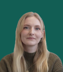 A headshot of Rachel Chalk. She has long blond hair and is wearing a dark green jumper. She is smiling whilst looking at the camera.